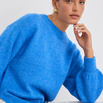 Model wears a azure blue long sleeve knit jumper with white jeans