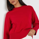 model wears a red knit jumper with white wide leg jeans