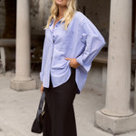 model wears a blue oversized shirt with a black skirt