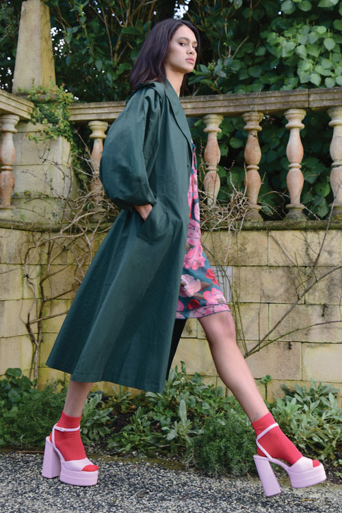 Model wears a green trench coat with a floral dress