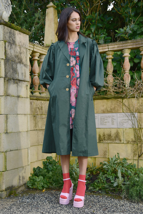 Model wears a green trench coat with a floral dress