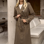 Woman wears a dark green khaki double breasted trench coat.