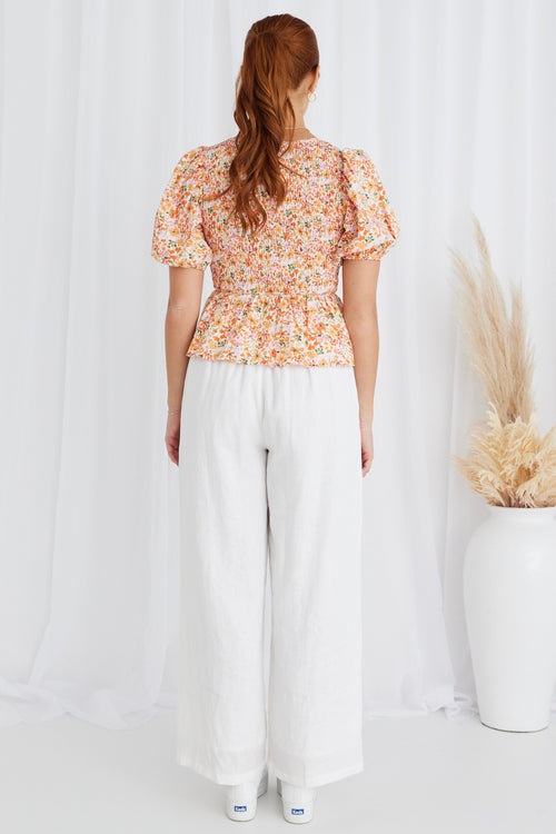 model in orange floral top and white pants and white sneakers