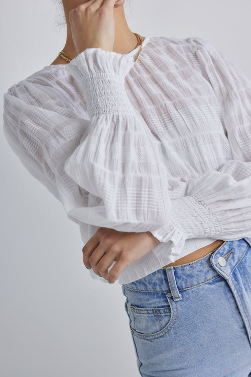 Model posing in white long sleeve cotton top and blue jeans