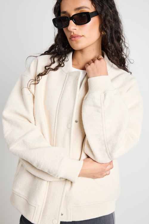 model wears a white bomber jacket with grey pants