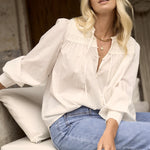 A woman wearing an ivory blouse with pintuck detailing, balloon sleeves with smocked cuffs, and a tie-front neckline, styled with light blue wide-leg jeans and leopard print heels.