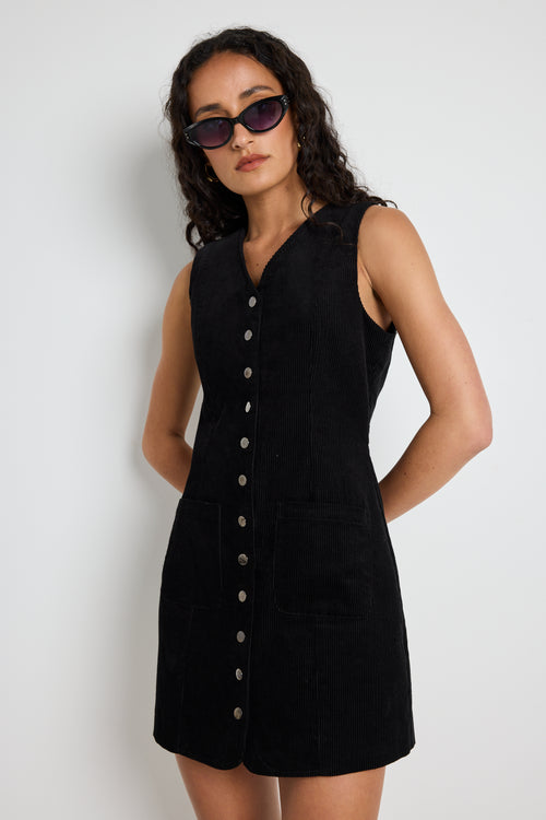 Model wears a black cord mini dress with silver buttons