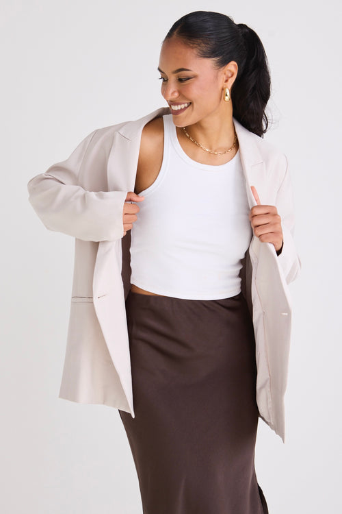 Model wears a bone blazer with a white singlet and skirt. 