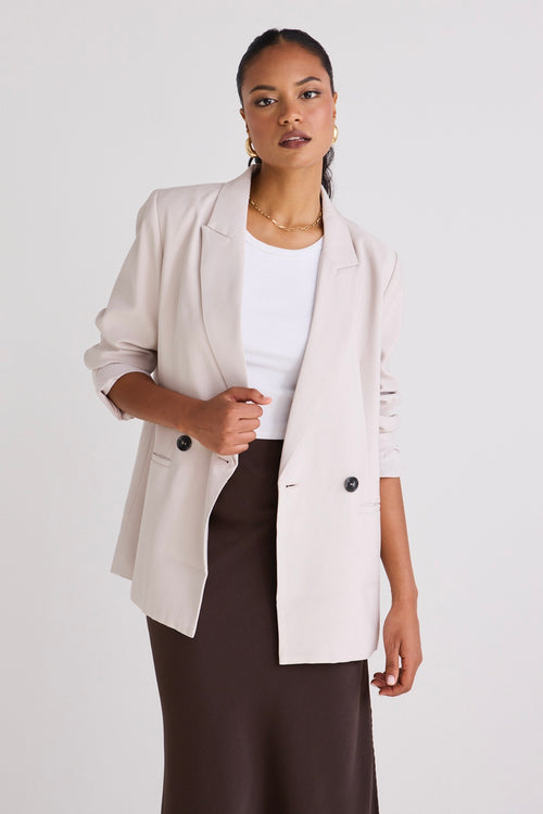 Model wears a bone blazer with a white singlet and skirt. 