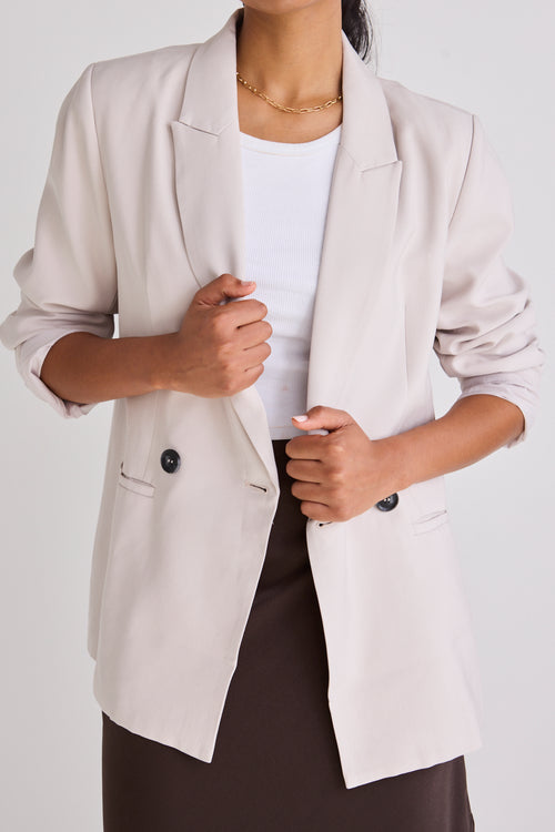 Model wears a bone blazer with a white singlet and skirt. 