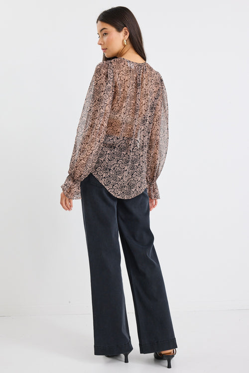 Woman wearing a sheer, long-sleeved floral blouse with balloon sleeves and black jeans