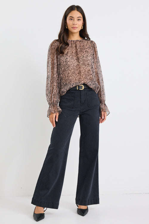 Woman wearing a sheer, long-sleeved floral blouse with balloon sleeves and black jeans