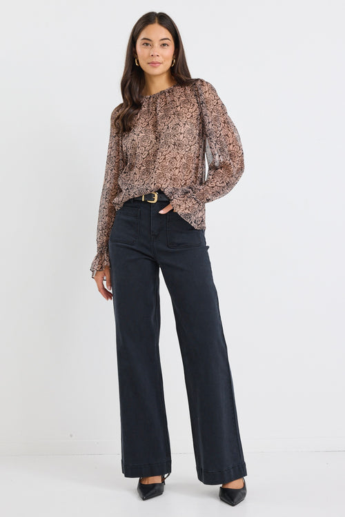Woman wearing a sheer, long-sleeved floral blouse with balloon sleeves and black jeans