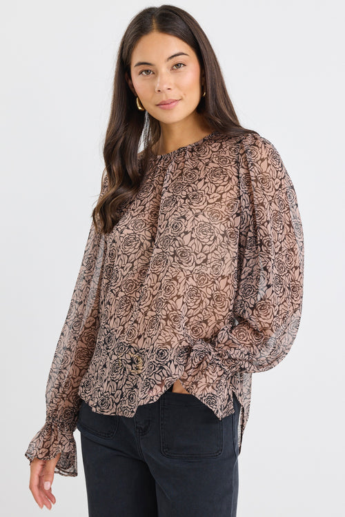 Woman wearing a sheer, long-sleeved floral blouse with balloon sleeves and black jeans