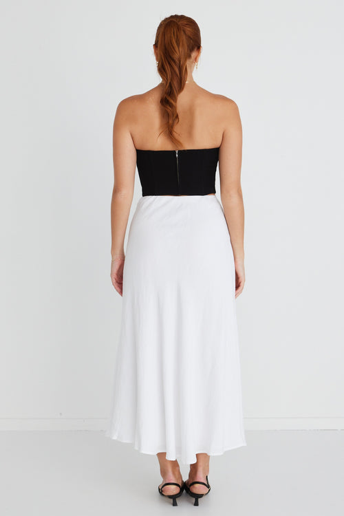 model wears a strapless black top with white midi skirt and black heels