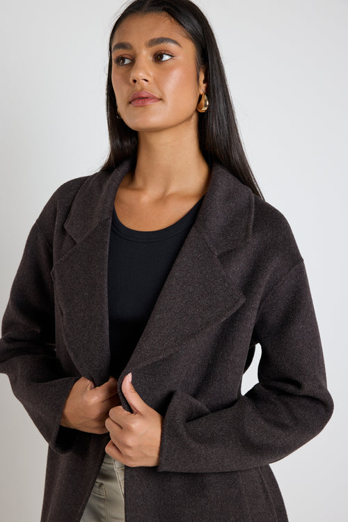 Woman wearing a chocolate brown longline coat over a black tank and cream wide-leg jeans.