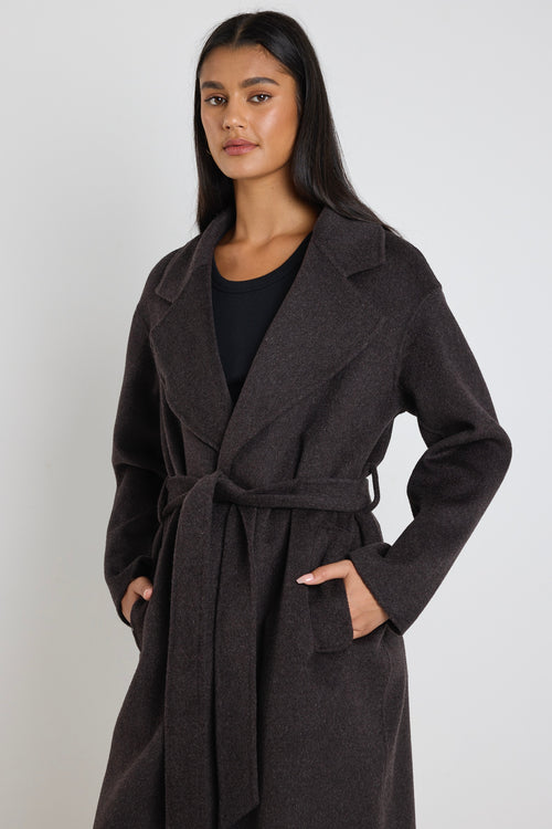 Woman wearing a chocolate brown longline coat over a black tank and cream wide-leg jeans.