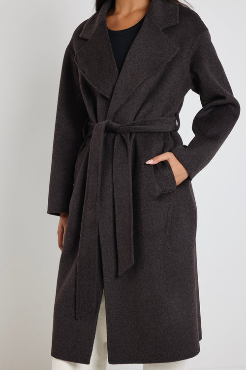 Woman wearing a chocolate brown longline coat over a black tank and cream wide-leg jeans.