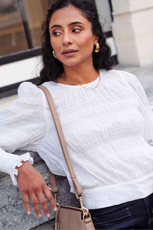 model wears a white cotton long sleeve top with blue jeans and a brown handbag