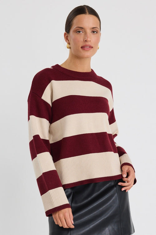 Woman wearing a burgundy and oatmeal striped jumper with long sleeves and a leather mini skirt.
