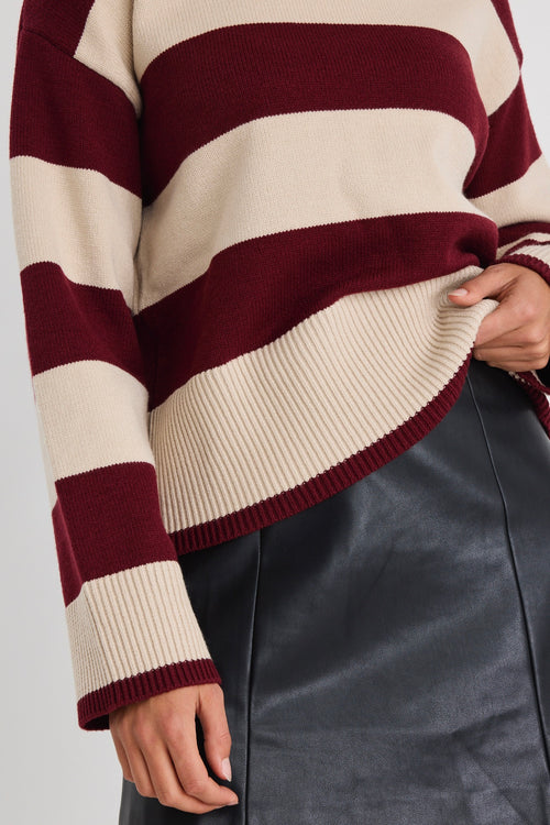 Woman wearing a burgundy and oatmeal striped jumper with long sleeves and a leather mini skirt.