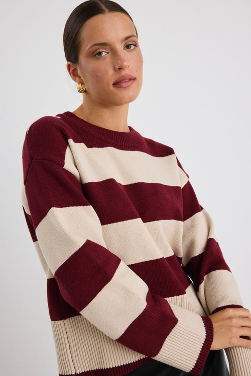 Woman wearing a burgundy and oatmeal striped jumper with long sleeves and a leather mini skirt.