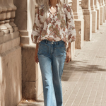 Model wears cream floral blouse and blue jeans