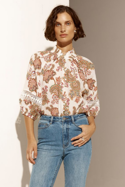 Model wears cream floral blouse and blue jeans