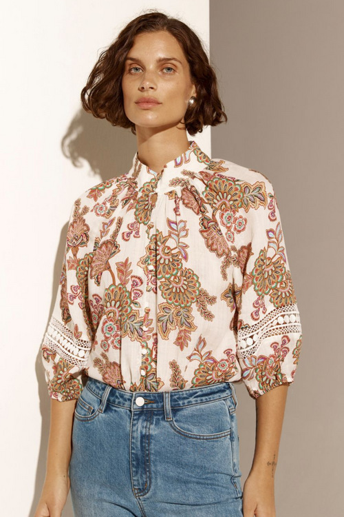 Model wears cream floral blouse and blue jeans