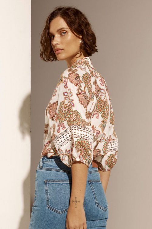 Model wears cream floral blouse and blue jeans