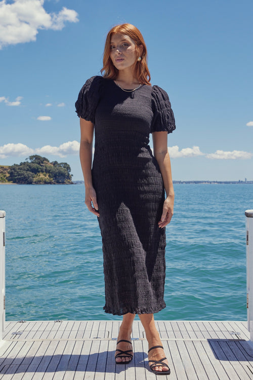 Model wears a black shirred cotton dress. 