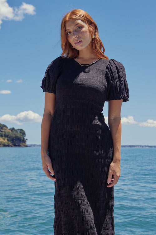 Model wears a black shirred cotton dress. 