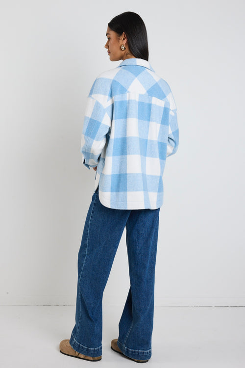 Model wears a blue check shacket with front pockets and a collar paired with blue jeans