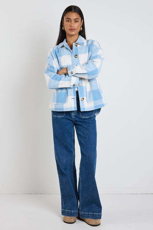 Model wears a blue check shacket with front pockets and a collar paired with blue jeans