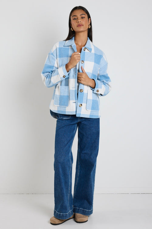 Model wears a blue check shacket with front pockets and a collar paired with blue jeans