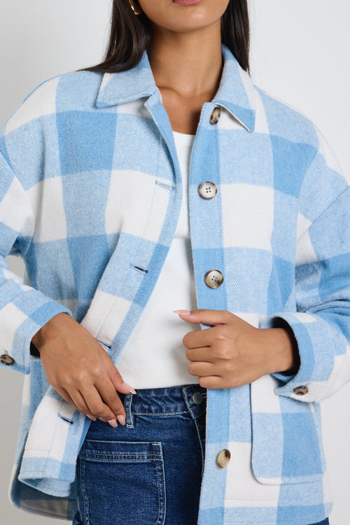 Model wears a blue check shacket with front pockets and a collar paired with blue jeans