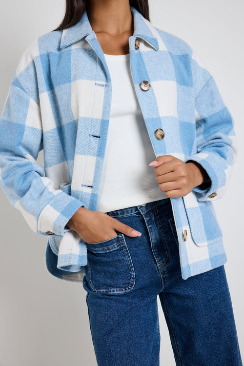 Model wears a blue check shacket with front pockets and a collar paired with blue jeans