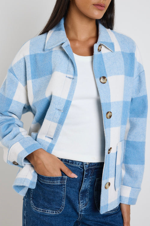 Model wears a blue check shacket with front pockets and a collar paired with blue jeans