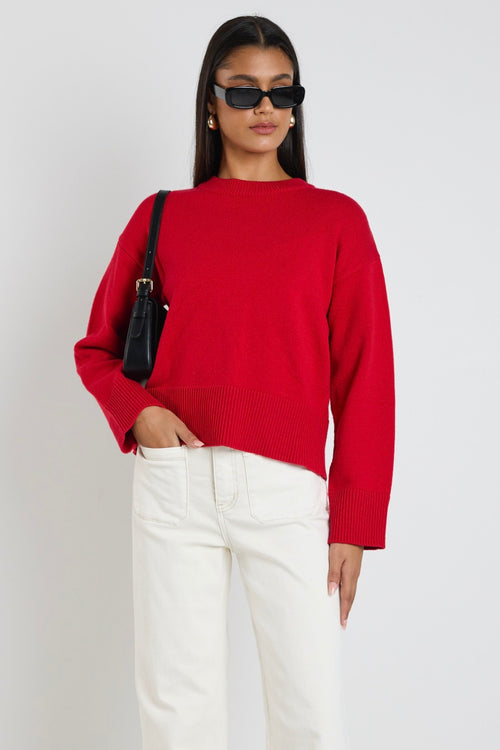 model wears a red knit jumper with white wide leg jeans