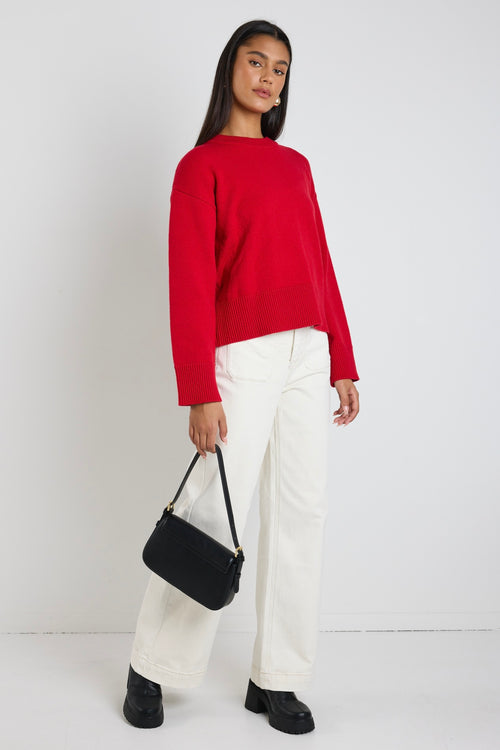 model wears a red knit jumper with white wide leg jeans