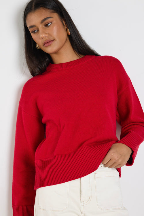 model wears a red knit jumper with white wide leg jeans