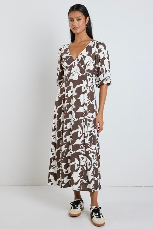 Model wears a brown pattern maxi dress with a v neckline. 