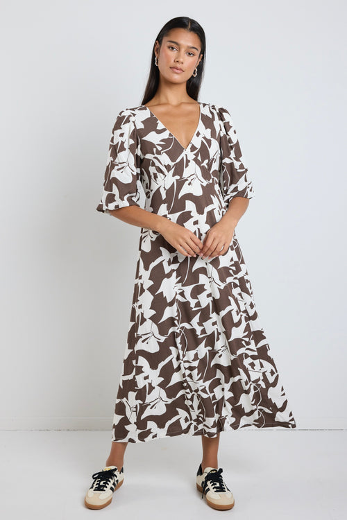 Model wears a brown pattern maxi dress with a v neckline. 