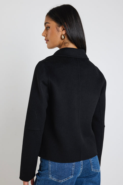 A woman wearing a black marle wool-blend cropped coat with gold buttons, styled with a beige tank top and blue jeans.