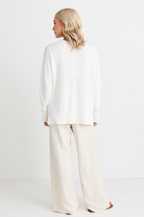 model wears natural linen pants and a white jumper and sandals