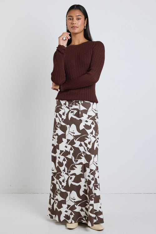 Model wears brown pattern maxi skirt with a tie waist and a long sleeve brown top. 