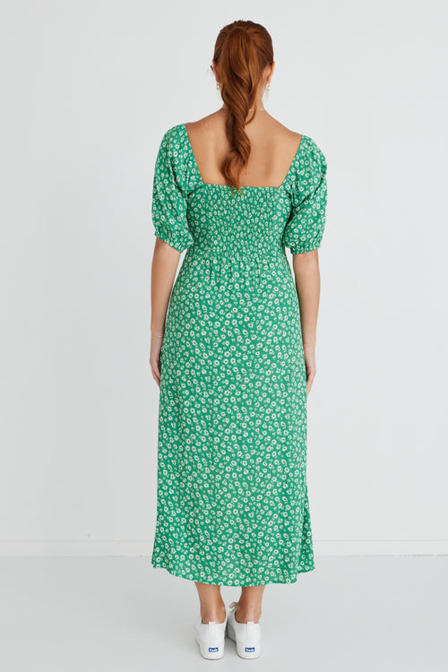 Model wears a green floral print maxi dress with white sneakers and a beige handbag.  