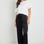 Woman wearing black Townie satin pants with a sandy beige side stripe, paired with a white tee for a sporty yet sophisticated look.