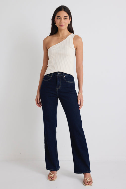 model wears dark blue jeans and one shoulder cream tp with beige heels