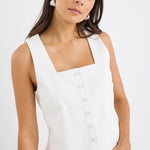 Woman wearing an ivory sleeveless linen vest with an off-centre button-down front, styled with blue jeans.